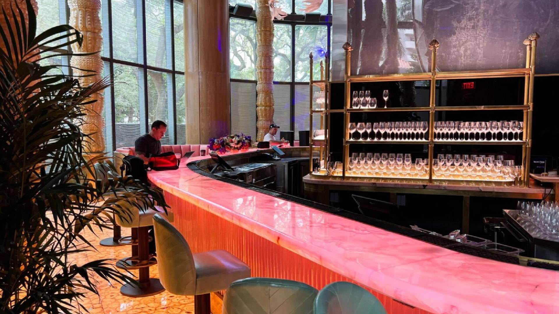 A bar with pink counter and chairs in front of a large window.