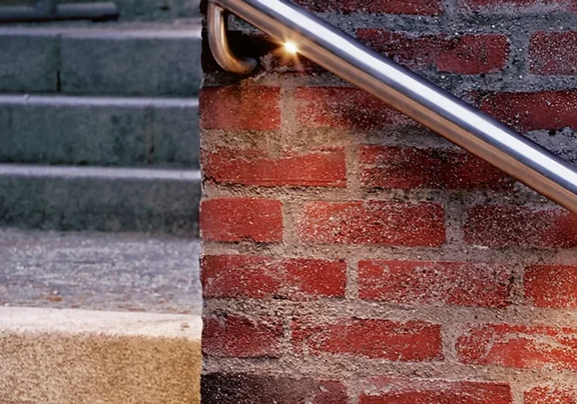 Close-up of a silver handrail attached to a red brick wall beside stone steps.