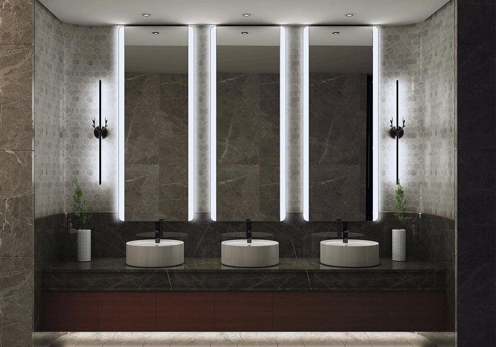 Modern restroom with three illuminated mirrors and sinks.