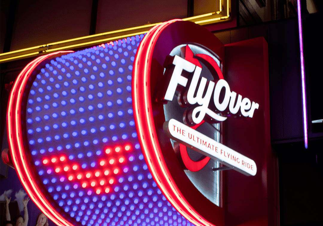 Illuminated FlyOver attraction sign glowing at night.