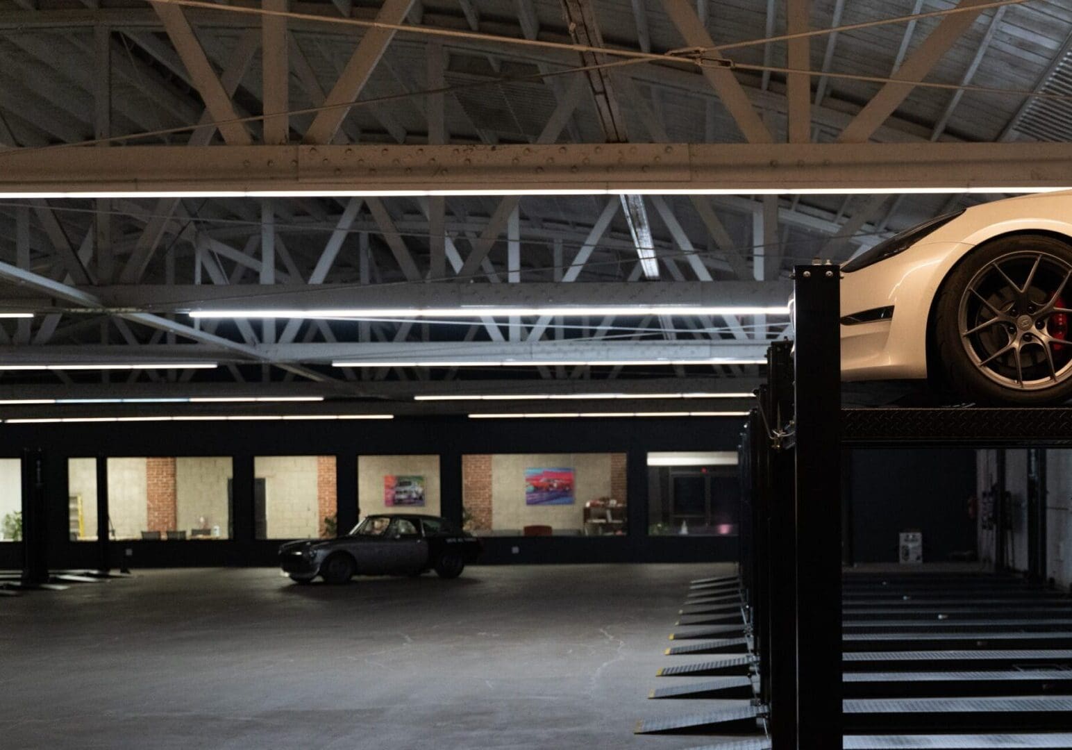 Dimly lit parking area with a single car and structural beams above.