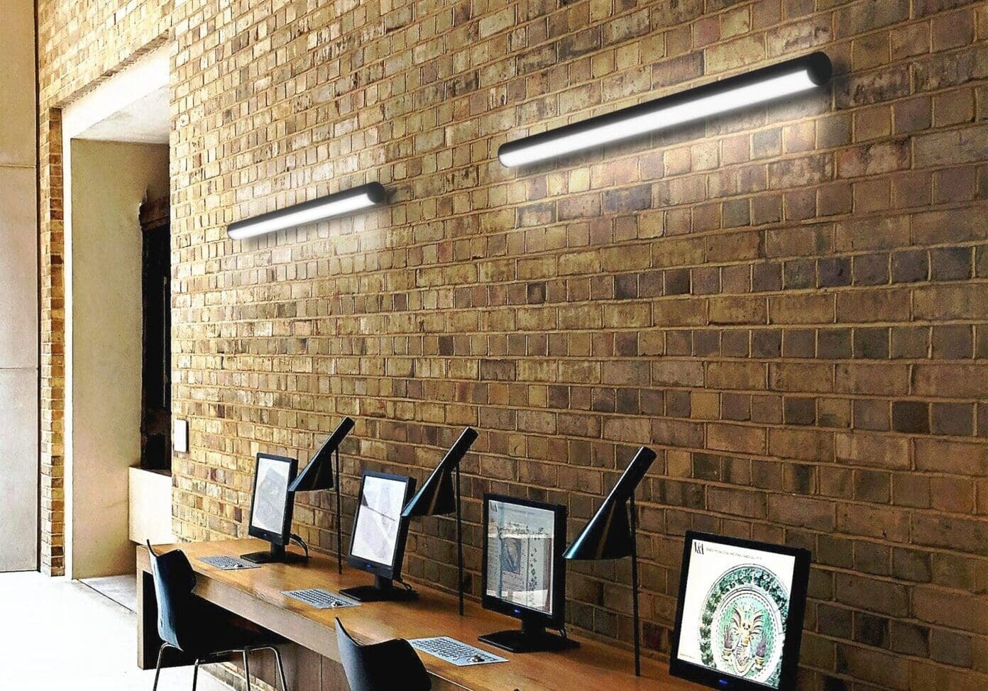 Modern workspace with computers against a brick wall and sleek lighting.